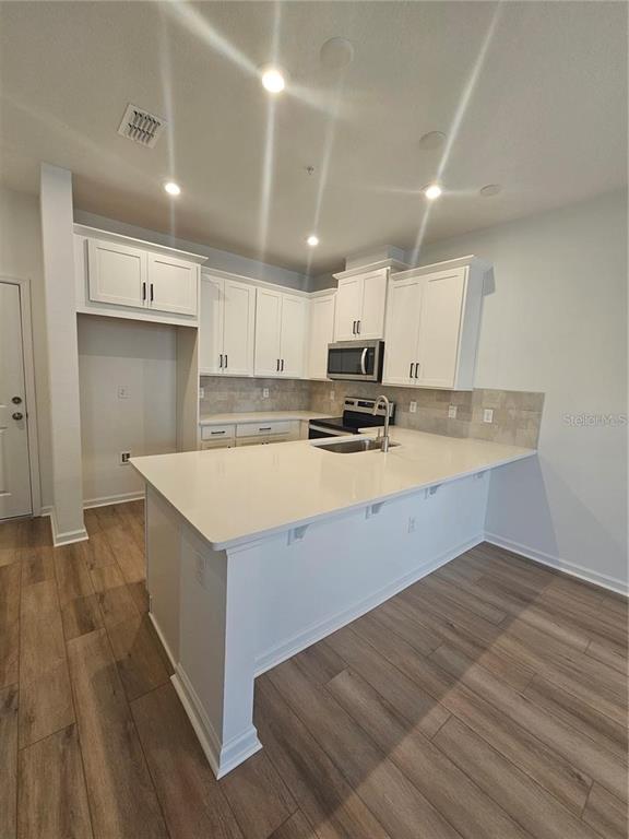 A modern kitchen features white cabinetry, a quartz island countertop, and light wood-look flooring — 11459 SUNSAIL AVENUE, ORLANDO, FL