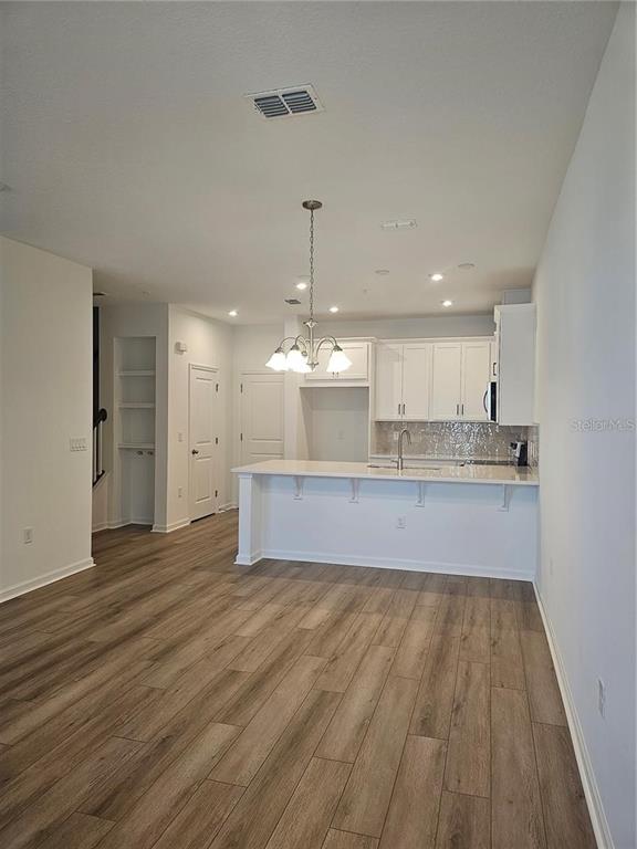A kitchen with white cabinets, a breakfast bar, and wood-look flooring in an open space — 11459 SUNSAIL AVENUE, ORLANDO, FL