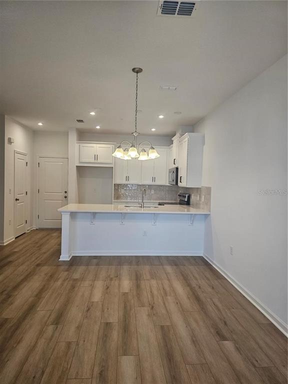 A kitchen with white cabinets, a breakfast bar, and wood-look flooring in an open space — 11459 SUNSAIL AVENUE, ORLANDO, FL