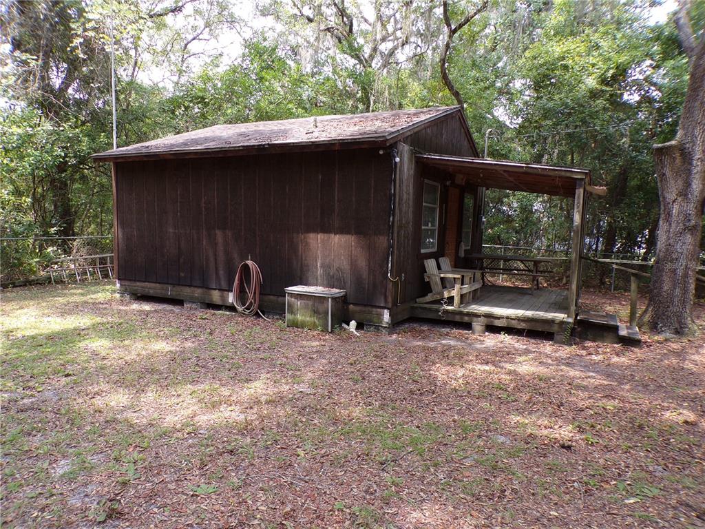A small, dark wood-sided cabin features a covered front porch and sits on a wooded lot — 30 NE 478TH AVENUE, OLD TOWN, FL