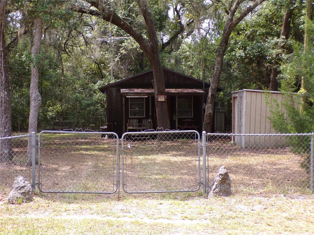A small, dark wood-sided cabin sits behind a chain-link fence in a wooded area — 30 NE 478TH AVENUE, OLD TOWN, FL