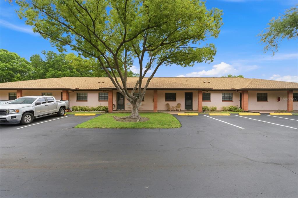 A single-story building with a tan exterior, a shingled roof, and a paved parking lot — 13250 RIDGE ROAD UNIT 7-4, LARGO, FL