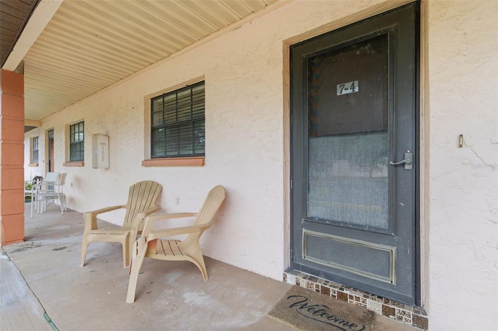 A covered exterior walkway features two plastic chairs, a window, and a dark screen door — 13250 RIDGE ROAD UNIT 7-4, LARGO, FL