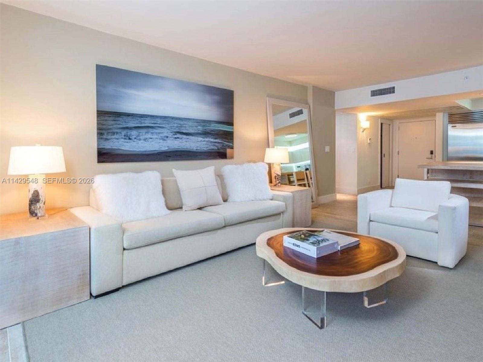 A room features a woven orange chair, a wooden bookshelf, and a balcony overlooking water — 102 24th St # 1006, Miami Beach FL 33139, MIAMI BEACH, FL