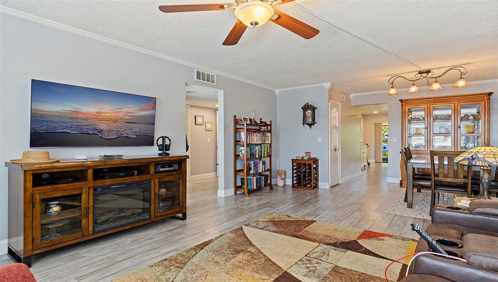A living room features a television console, a bookshelf, and a dining area beyond — 4910 BAY STREET NE UNIT 310, ST PETERSBURG, FL