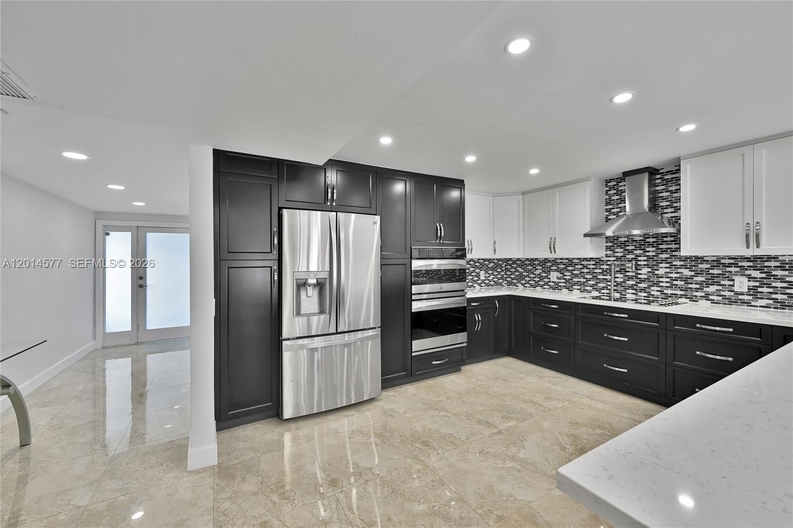 A modern kitchen features two-tone cabinets, stainless steel appliances, and light-colored tile flooring — SUNNY ISLES BEACH, FL