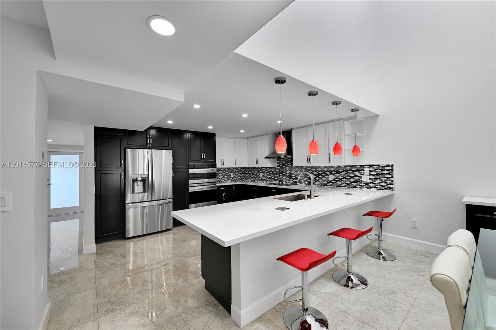 A modern kitchen features black and white cabinetry, a white island, and red bar stools — SUNNY ISLES BEACH, FL
