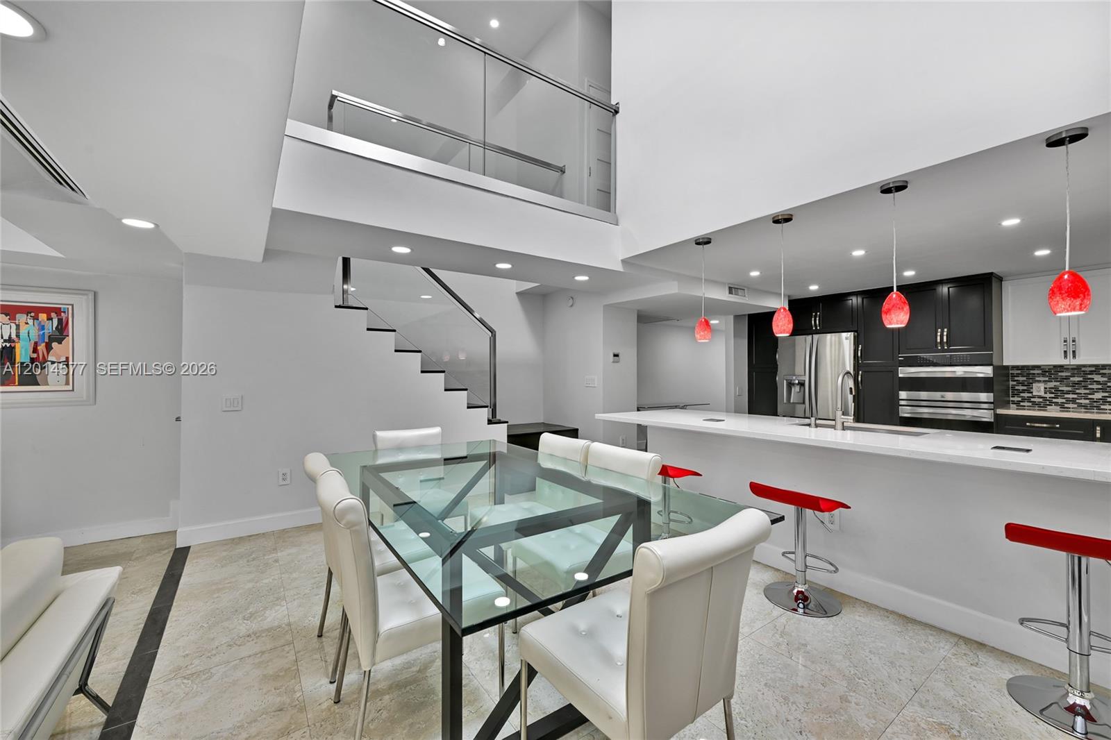 A modern dining area and kitchen feature a glass table, white chairs, and red stools — SUNNY ISLES BEACH, FL