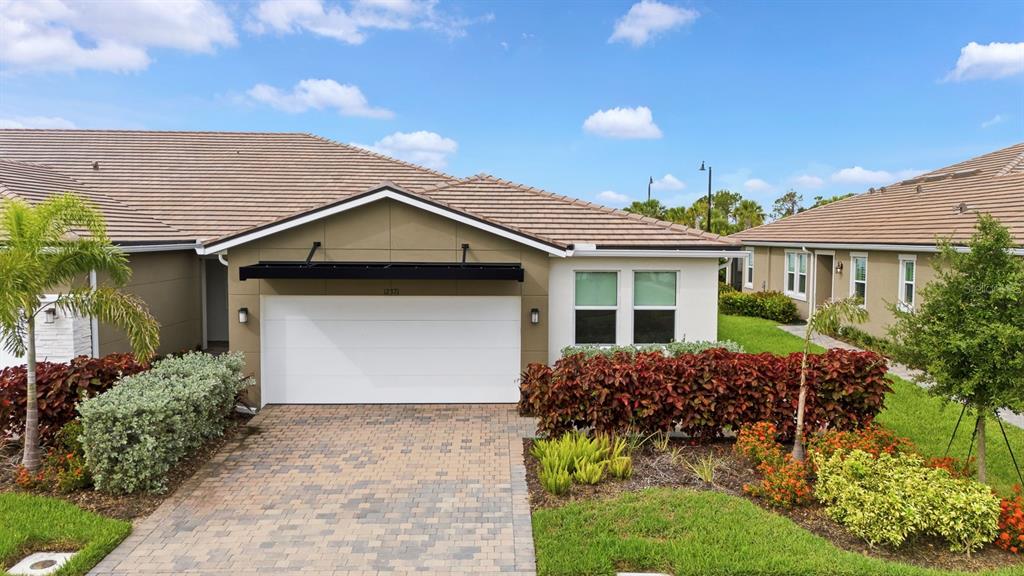 A single-story house exterior features a white garage door, tan siding, and a tiled roof — 12371 HEARTS EASE ST, VENICE, FL