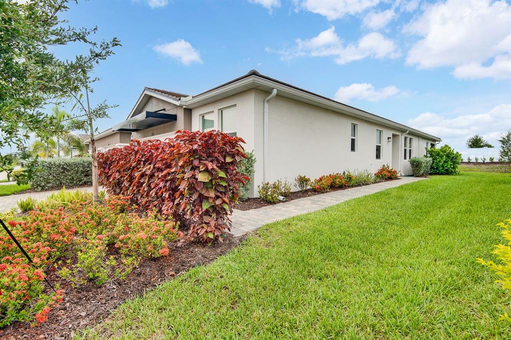 A side view of a beige house exterior with a paved walkway and landscaped garden — 12371 HEARTS EASE ST, VENICE, FL