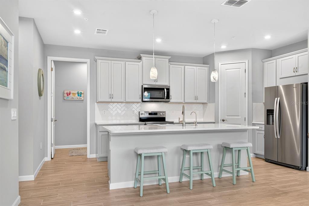 A kitchen features light gray cabinets, a white island with three stools, and stainless appliances — 12371 HEARTS EASE ST, VENICE, FL