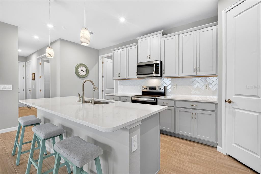 A modern kitchen features light gray cabinets, a white quartz island, and three bar stools — 12371 HEARTS EASE ST, VENICE, FL