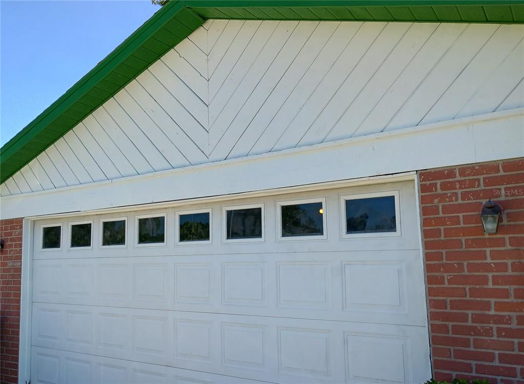 A white garage door is positioned below a white gable with diagonal siding — 602 BAY LAKE TRAIL, OLDSMAR, FL