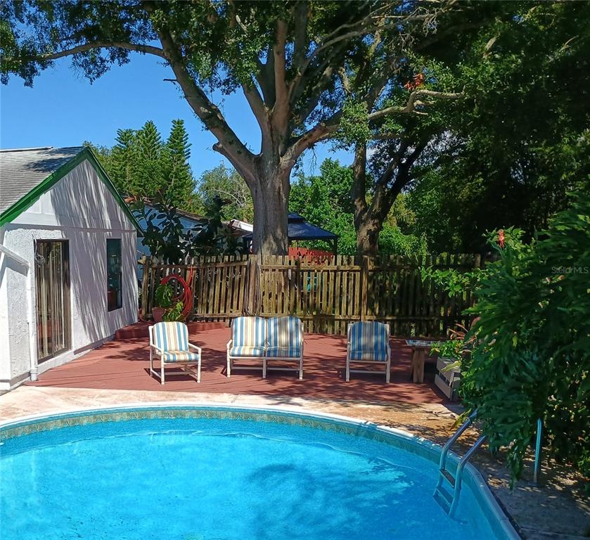 A backyard features a swimming pool, a red deck with patio furniture, and large trees — 602 BAY LAKE TRAIL, OLDSMAR, FL