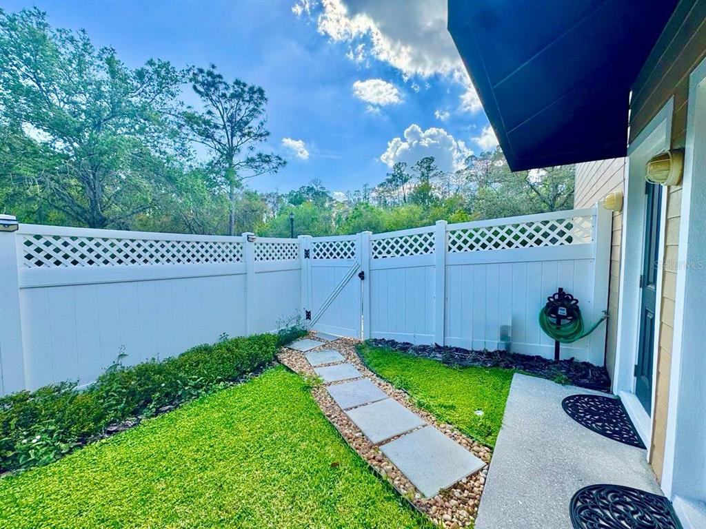 A fenced backyard features a stone path, green grass, and a door to the house — 14541 COTSWOLDS DRIVE UNIT B, TAMPA, FL