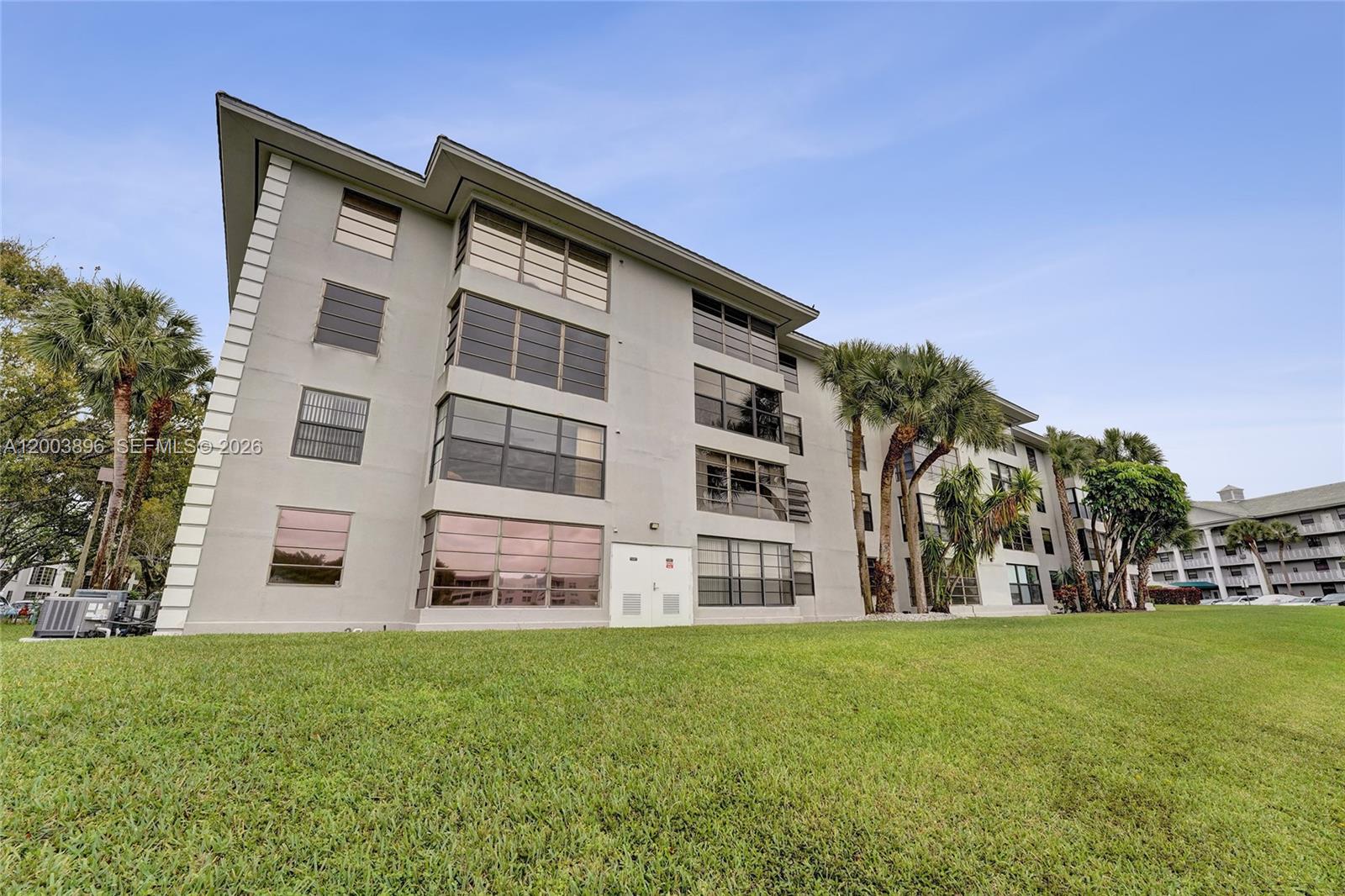 The exterior of a multi-story apartment building features light-colored walls, large windows, and palm trees — 1530 Whitehall Dr # 302, Davie FL 33324, DAVIE, FL