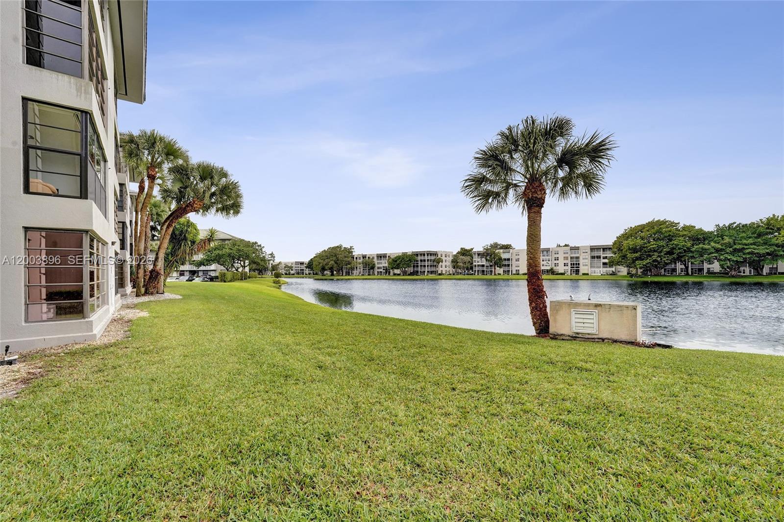 A grassy lawn extends from a multi-story building toward a lake with palm trees — 1530 Whitehall Dr # 302, Davie FL 33324, DAVIE, FL