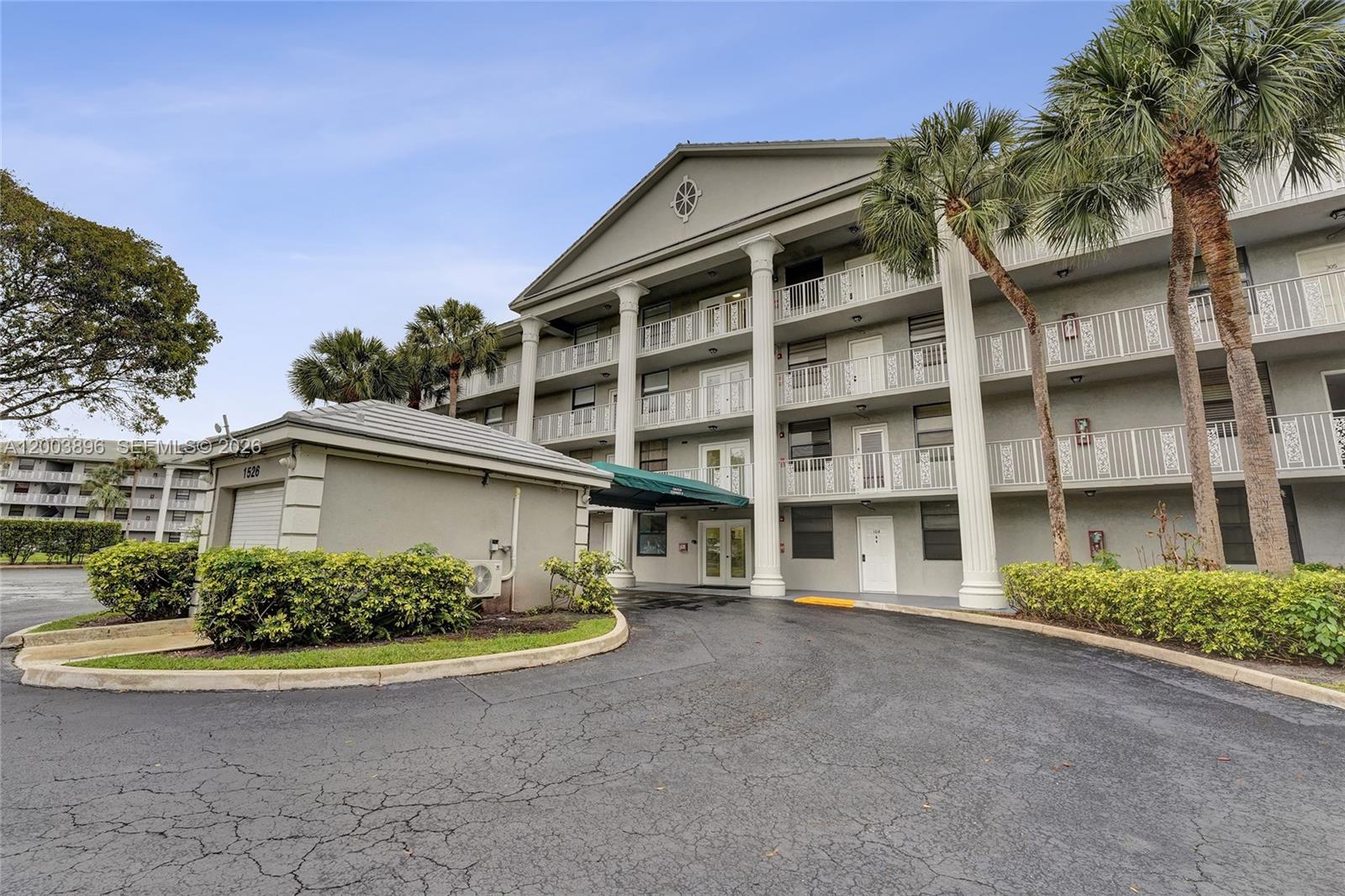 A multi-story apartment building features a covered entrance, white columns, and palm trees — 1530 Whitehall Dr # 302, Davie FL 33324, DAVIE, FL