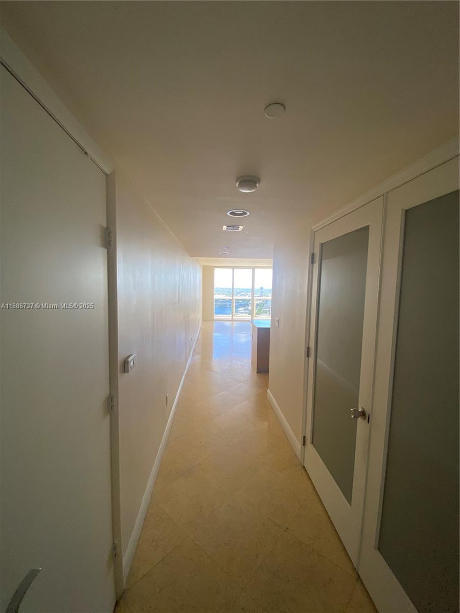 A narrow hallway with light-colored tile flooring leads toward a window with a city view — 1800 S Ocean Dr # 2909, Hallandale Beach FL 33009, HALLANDALE BEACH, FL