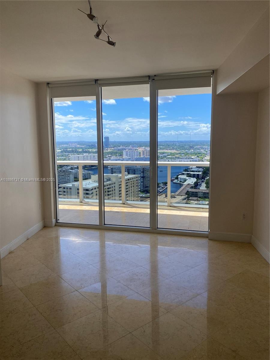 A room with beige tile floors and floor-to-ceiling windows overlooking a city and water — 1800 S Ocean Dr # 2909, Hallandale Beach FL 33009, HALLANDALE BEACH, FL