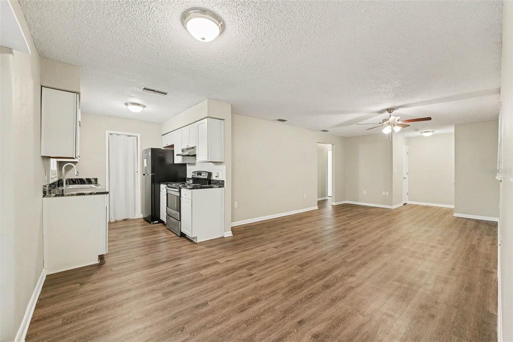 An open-concept kitchen and living area with white cabinets, black appliances, and wood-look flooring — 2047 SOMERVILLE DRIVE N, LAKELAND, FL
