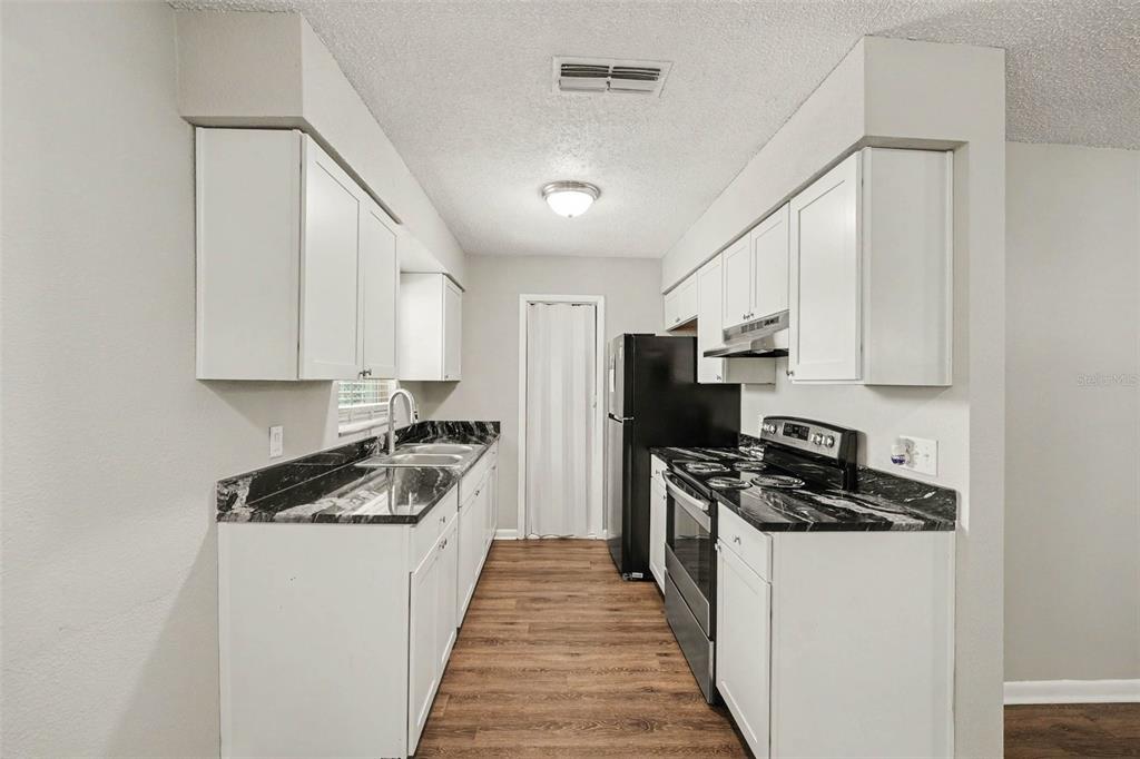 A galley kitchen features white cabinets, black countertops, and stainless steel appliances — 2047 SOMERVILLE DRIVE N, LAKELAND, FL