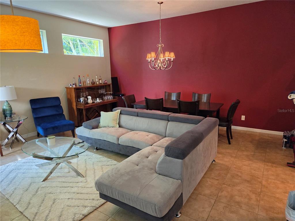 A living and dining area features a gray sectional sofa, a red accent wall, and tile flooring — 98 S HIGHLAND AVENUE UNIT 2002, TARPON SPRINGS, FL