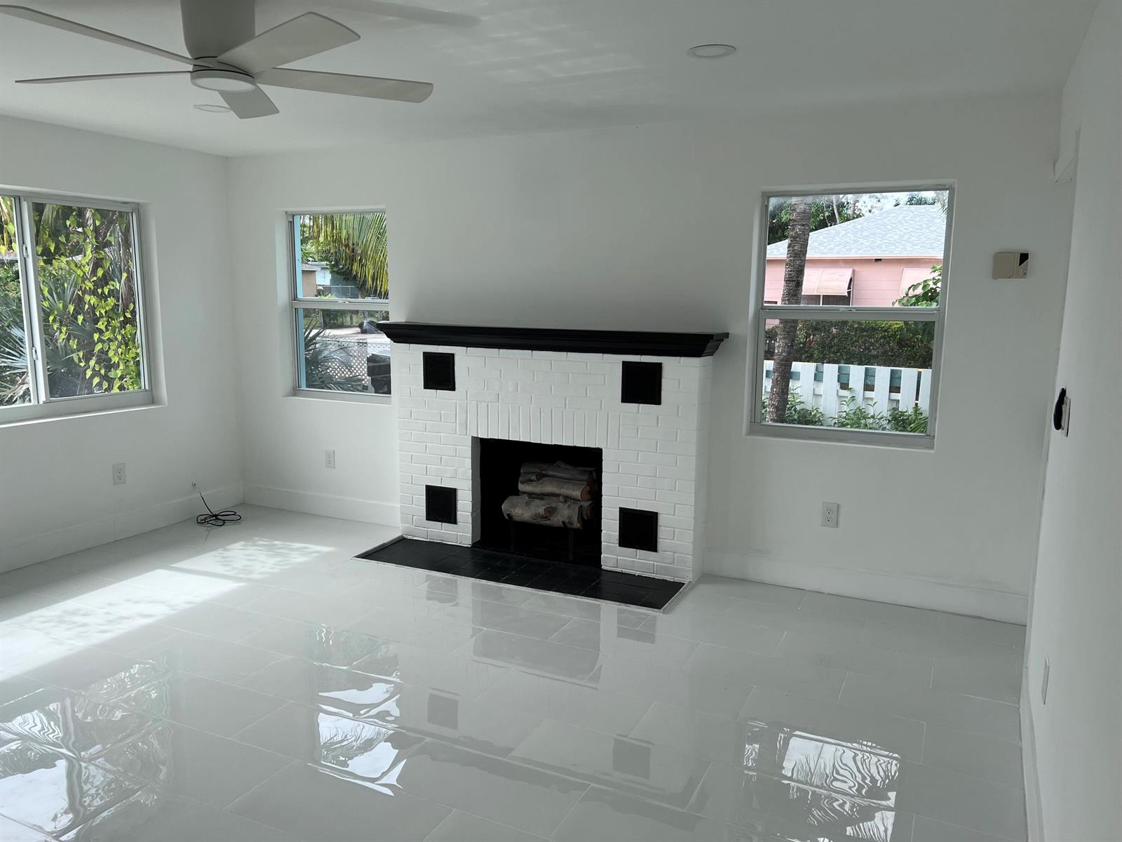 A bright living room features white tile floors, a white brick fireplace, and three windows — 1015 S K Street, FL 33460, FL