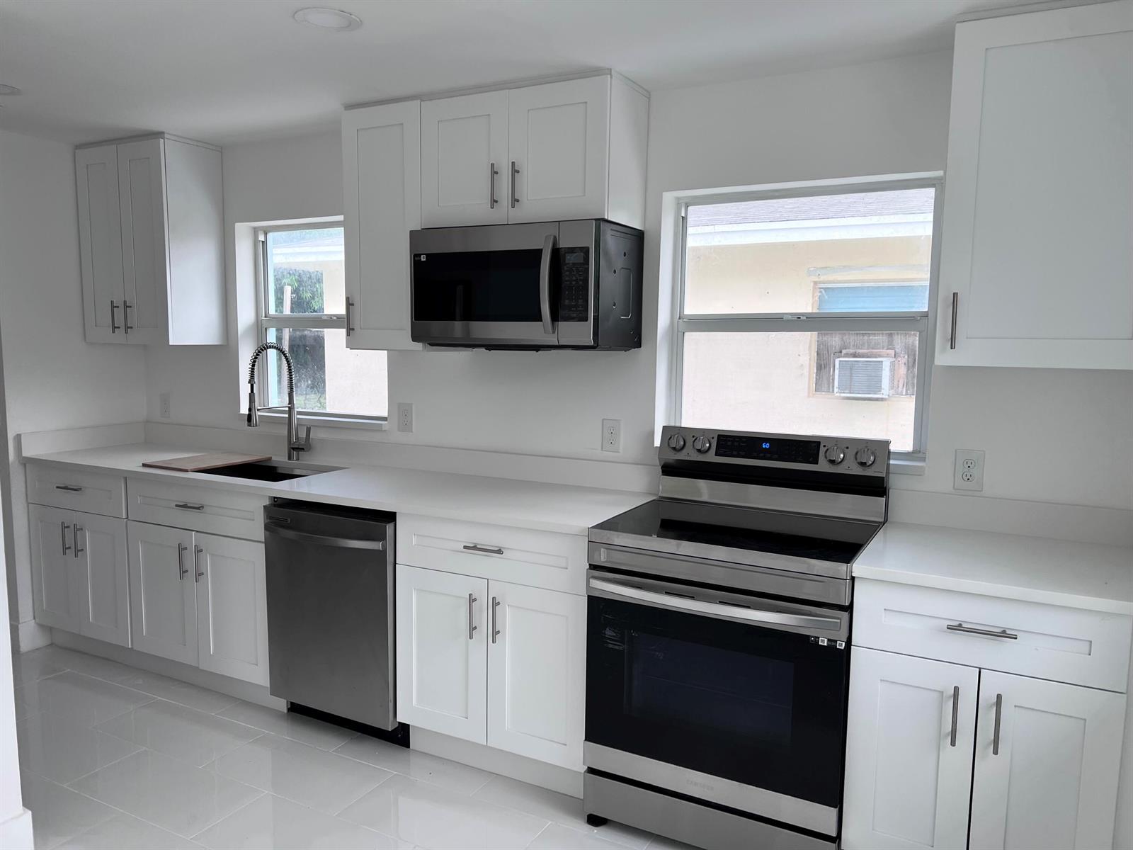A modern kitchen featuring white cabinets, stainless steel appliances, and white countertops — 1015 S K Street, FL 33460, FL
