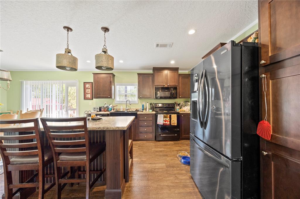 A kitchen features dark wood cabinetry, stainless steel appliances, a granite-topped island, and pendant lighting — 221 MAGNOLIA ROAD, HAWTHORNE, FL