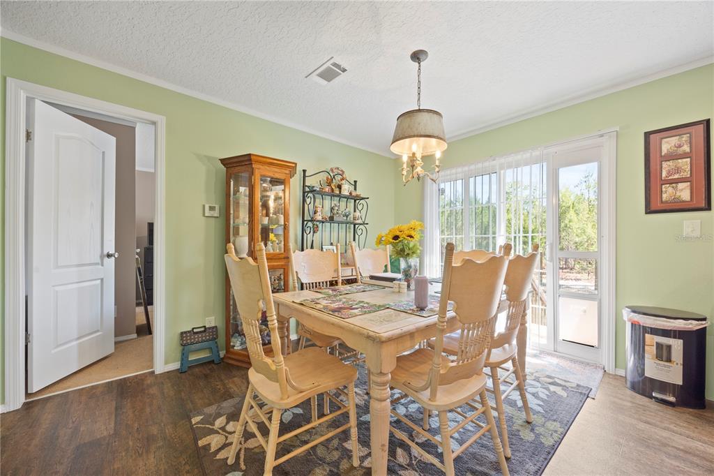 A dining room features light green walls, a wooden table with chairs, and sliding glass doors — 221 MAGNOLIA ROAD, HAWTHORNE, FL
