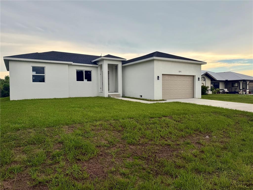 A single-story white house with a dark roof and a tan garage door — 571 MIMOSA AVENUE NW, PORT CHARLOTTE, FL