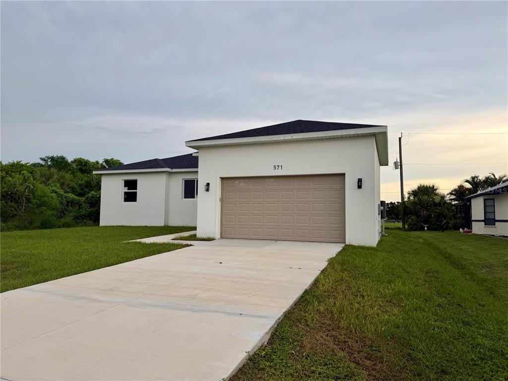A single-story house with a white stucco exterior, a tan garage door, and a concrete driveway — 571 MIMOSA AVENUE NW, PORT CHARLOTTE, FL