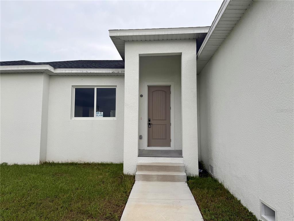 A white stucco house exterior features a recessed front entrance with concrete steps and walkway — 571 MIMOSA AVENUE NW, PORT CHARLOTTE, FL