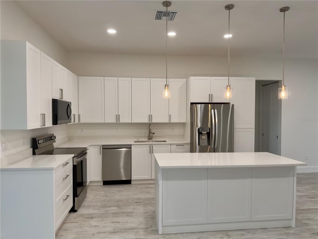 A modern kitchen features white cabinets, stainless steel appliances, a center island, and light flooring — 571 MIMOSA AVENUE NW, PORT CHARLOTTE, FL