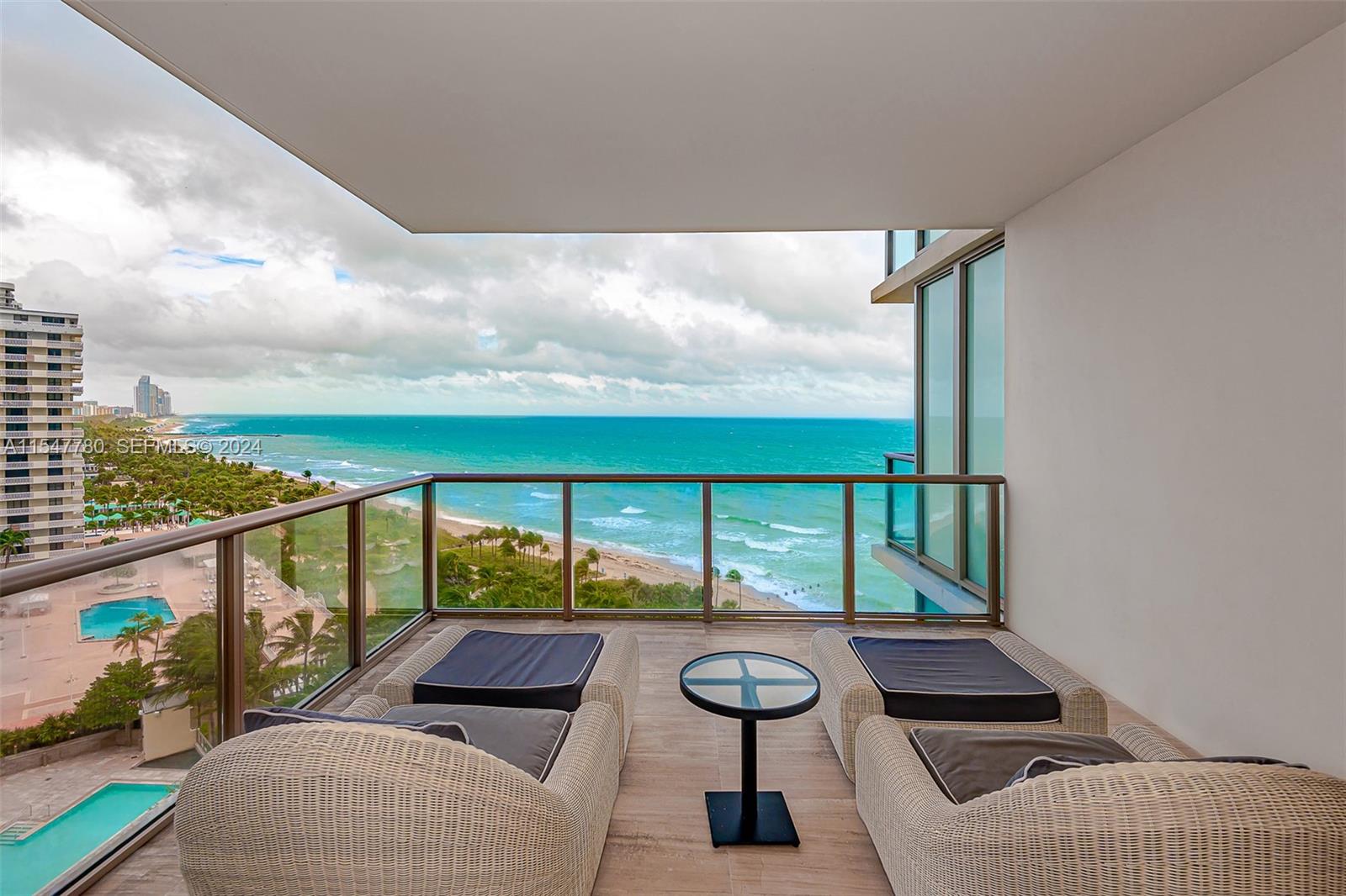 A balcony with two wicker lounge chairs and a small table overlooks the ocean — 9703 Collins Ave # 1001, Bal Harbour FL 33154, BAL HARBOUR, FL