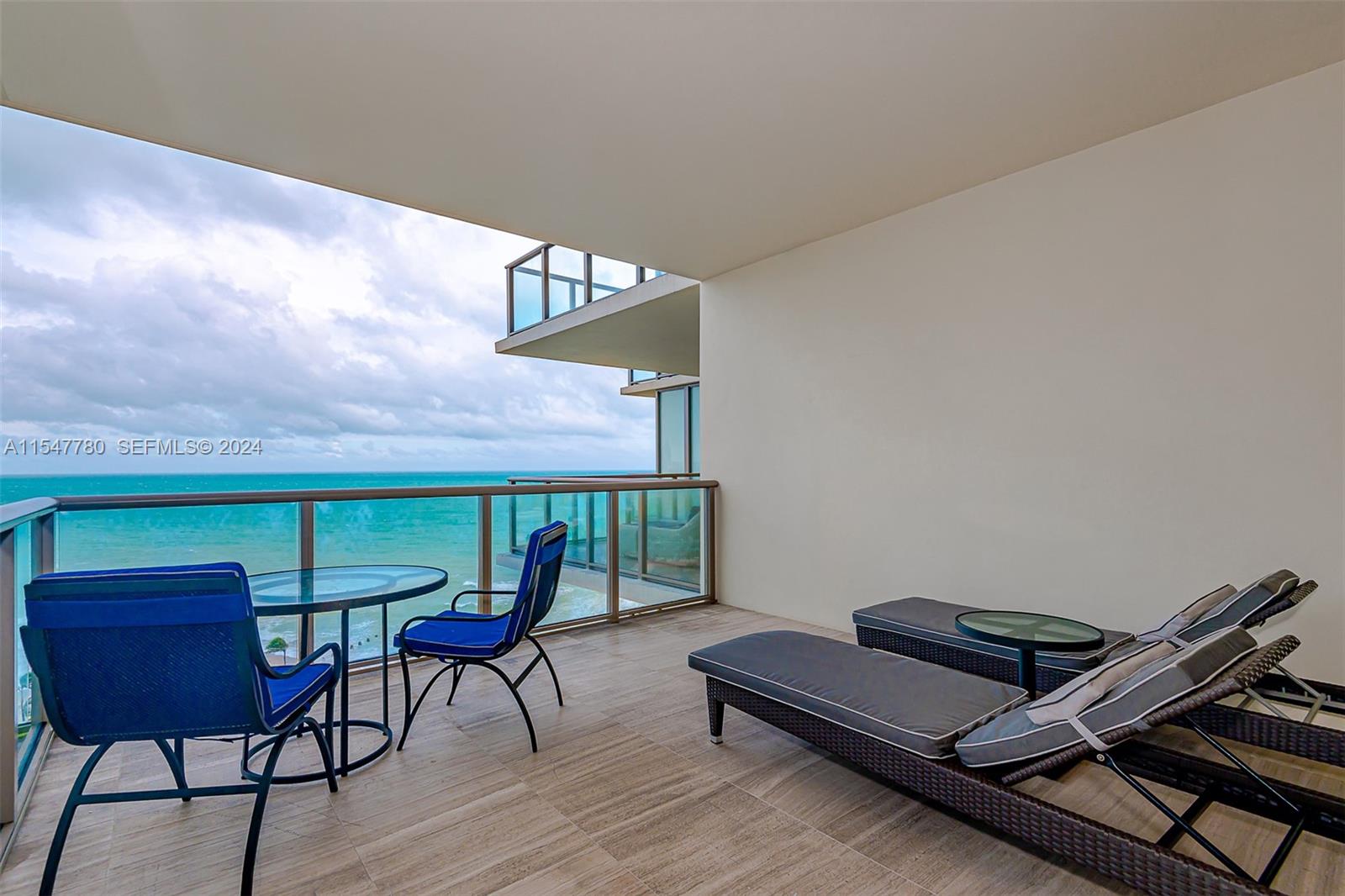 A balcony features a glass table, two blue chairs, and two lounge chairs overlooking the ocean — 9703 Collins Ave # 1001, Bal Harbour FL 33154, BAL HARBOUR, FL