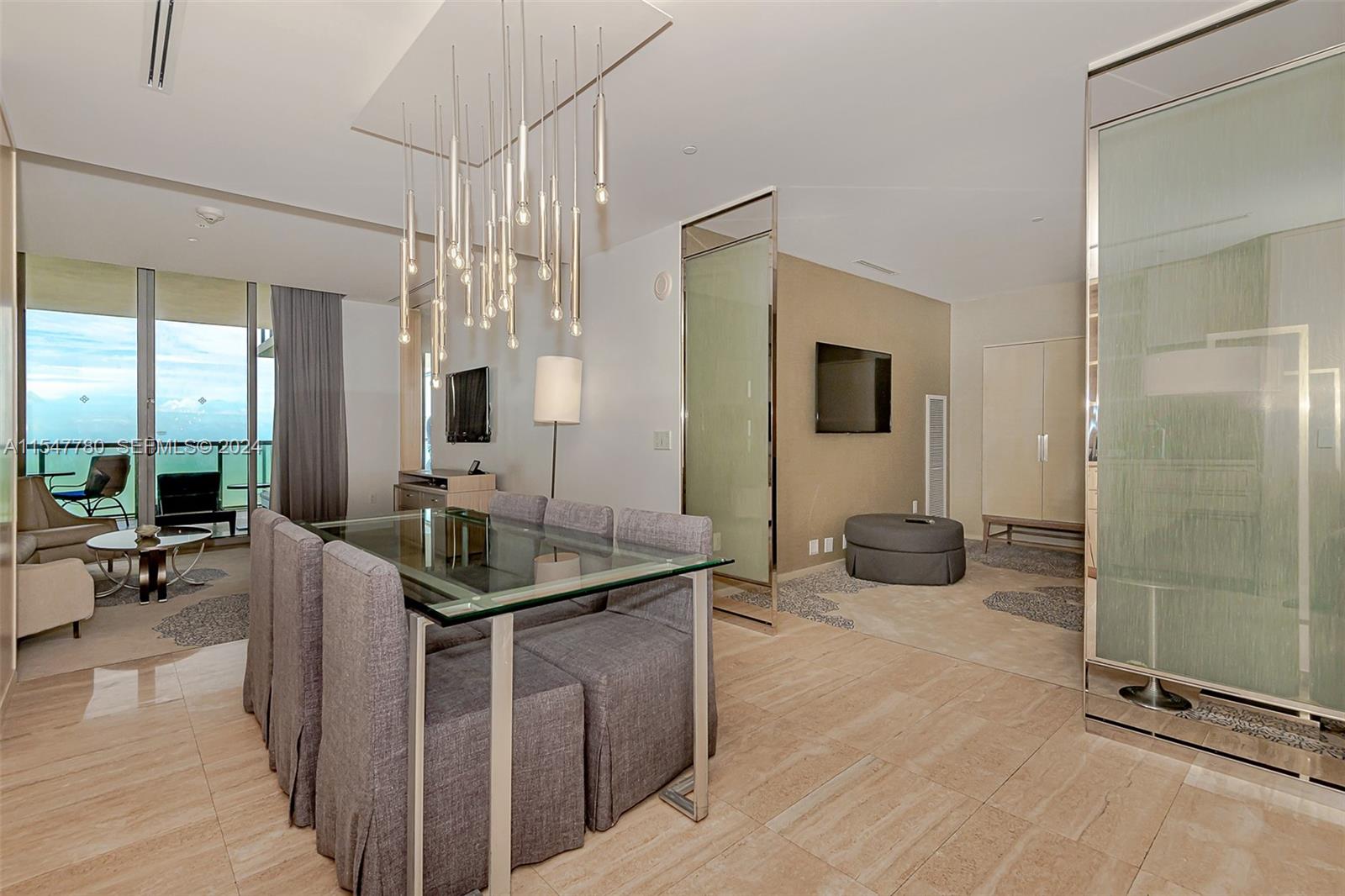 A dining area with a glass table and chandelier opens to a living space with balcony views — 9703 Collins Ave # 1001, Bal Harbour FL 33154, BAL HARBOUR, FL