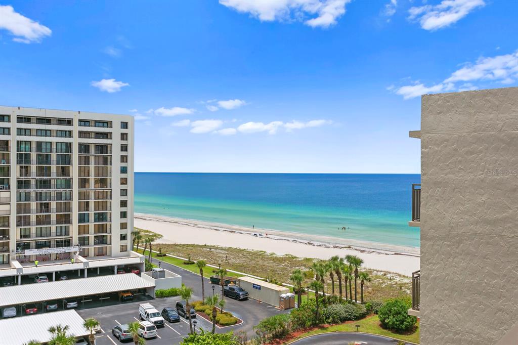 An elevated view shows a beach, the ocean, a parking lot, and a tall building — 1430 GULF BOULEVARD UNIT 806, CLEARWATER, FL