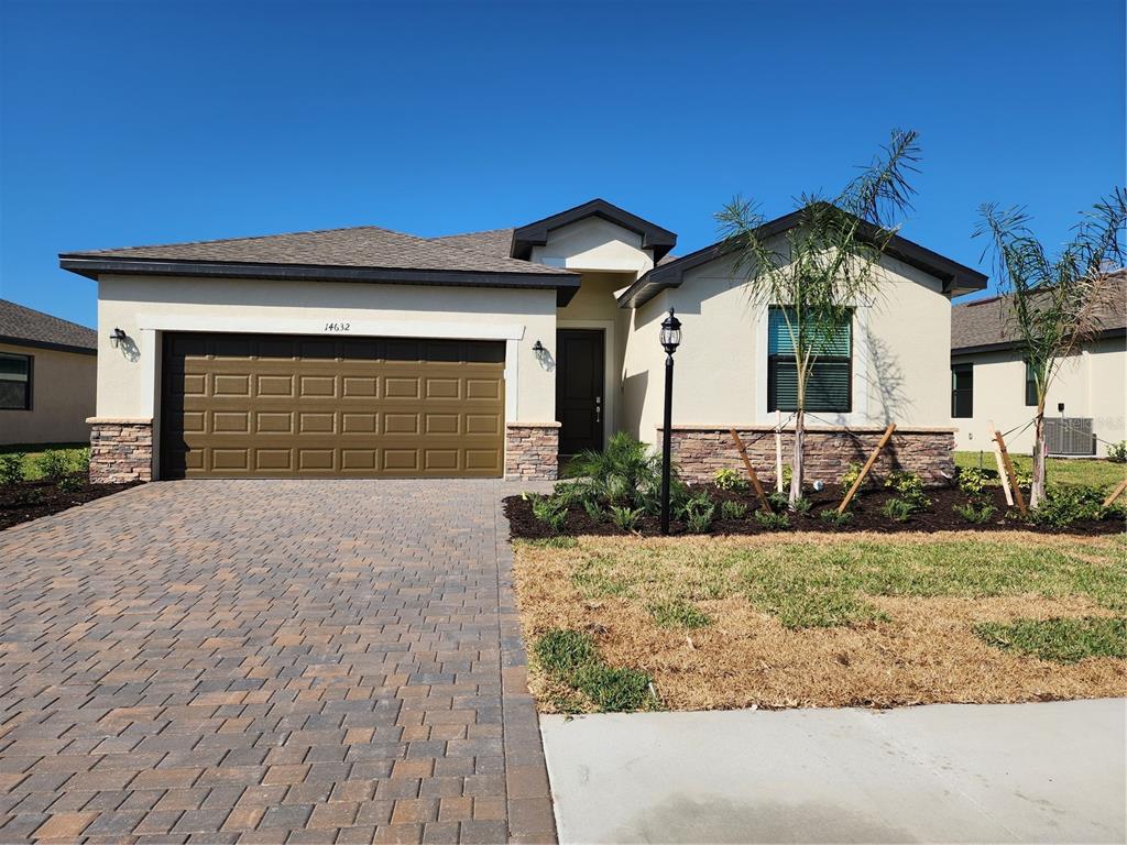 A single-story house features a paved driveway, a two-car garage, and stone veneer accents — 14632 PALAMOS CIRCLE, FORT MYERS, FL