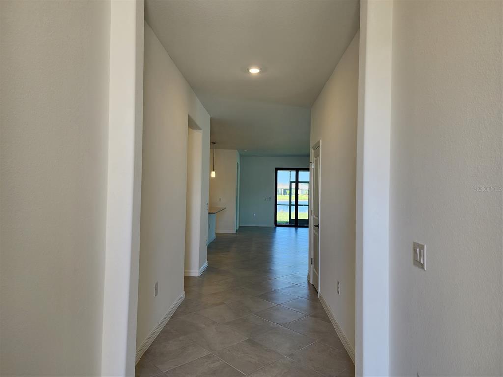 A tiled hallway leads to an open living area with a view of a lake — 14632 PALAMOS CIRCLE, FORT MYERS, FL