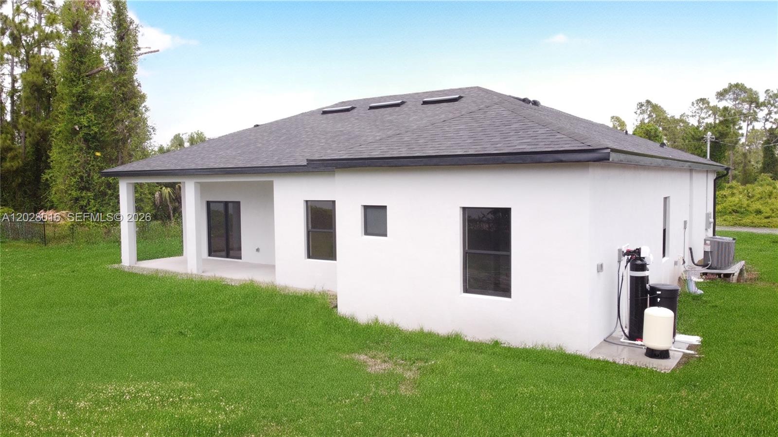 The exterior of a white stucco house features a covered patio and water treatment equipment — 7511 Blutter Rd, North Port FL 34291, NORTH PORT, FL