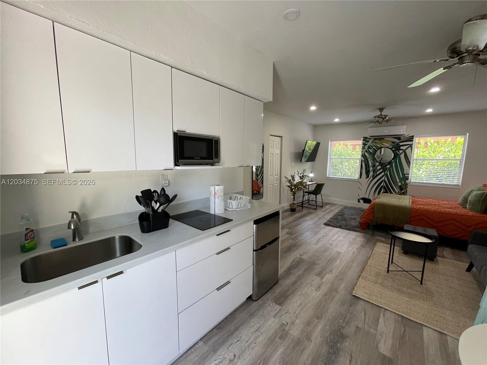 A studio apartment features a white kitchen, wood-look flooring, and a bedroom area — MIAMI, FL