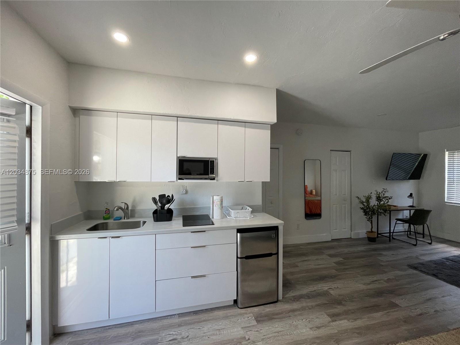 A kitchen with white cabinets, stainless steel appliances, and wood-look flooring in an open space — MIAMI, FL