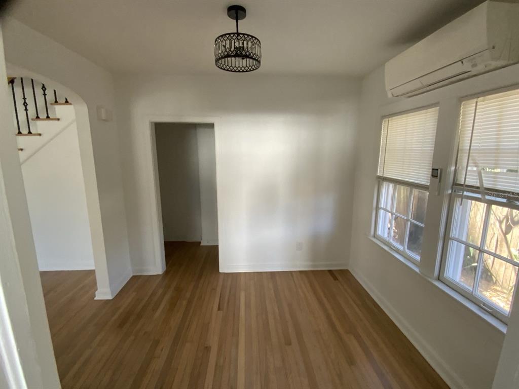 An empty room features hardwood floors, a dark metal light fixture, and a wall-mounted air conditioner — 608 HIGHLAND AVENUE, ORLANDO, FL