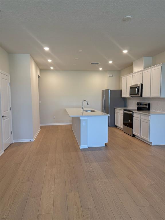 A kitchen features white cabinetry, a center island with a sink, and light wood flooring — 6406 TABEBUIA PARKWAY, WINTER GARDEN, FL