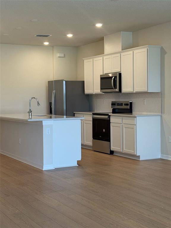 A kitchen features white cabinets, stainless steel appliances, and a central island with a sink — 6406 TABEBUIA PARKWAY, WINTER GARDEN, FL