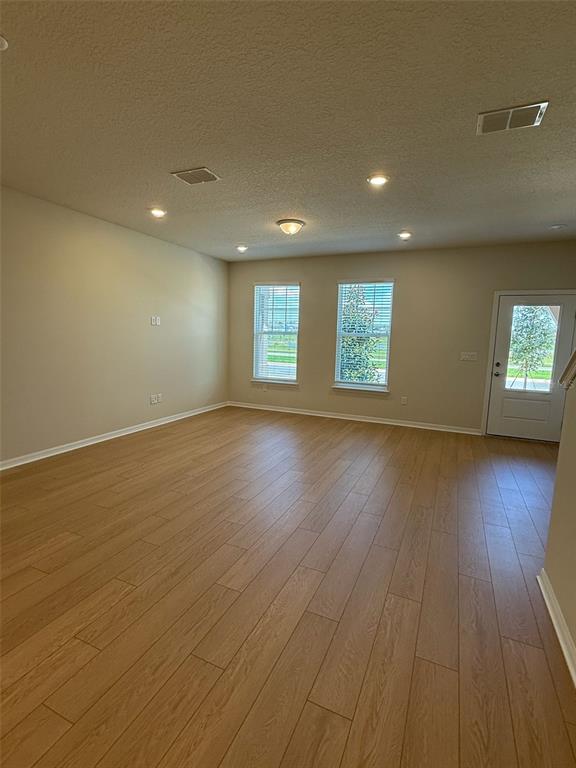 An empty living room features light wood-look flooring, recessed lighting, and two windows — 6406 TABEBUIA PARKWAY, WINTER GARDEN, FL