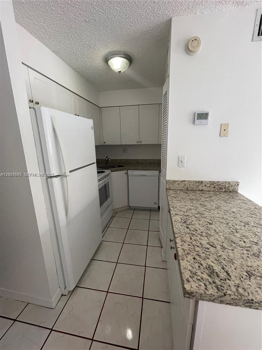 A galley kitchen features white cabinets, granite countertops, white appliances, and tiled flooring — 5199 NW 7th St # 112, Miami FL 33126, MIAMI, FL