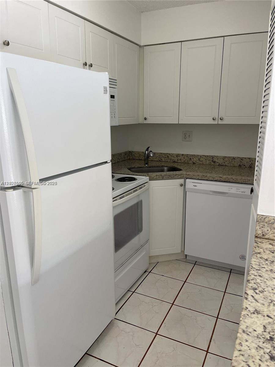A small kitchen features white cabinets, white appliances, and speckled granite countertops — 5199 NW 7th St # 112, Miami FL 33126, MIAMI, FL